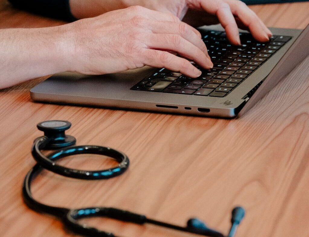 Arts stelt achter een laptop het medisch advies op na een consult, met een stethoscoop op tafel